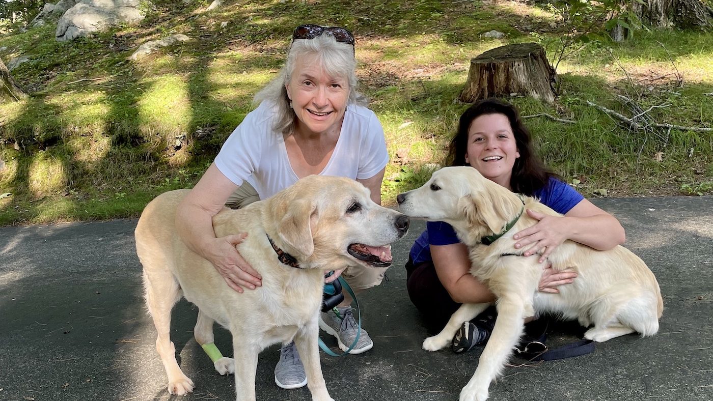 Mother/daughter pet sitting team sitting with an older Labrador and a young golden retriever.